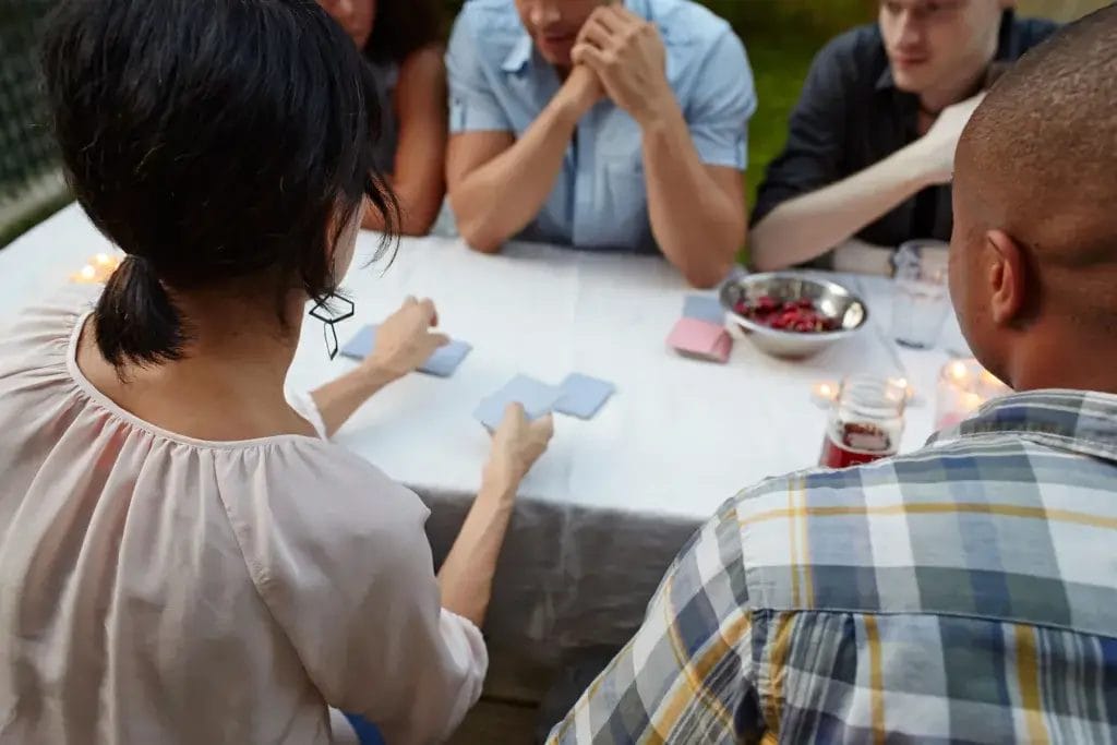 Friends sitting at a picnic table playing card games.