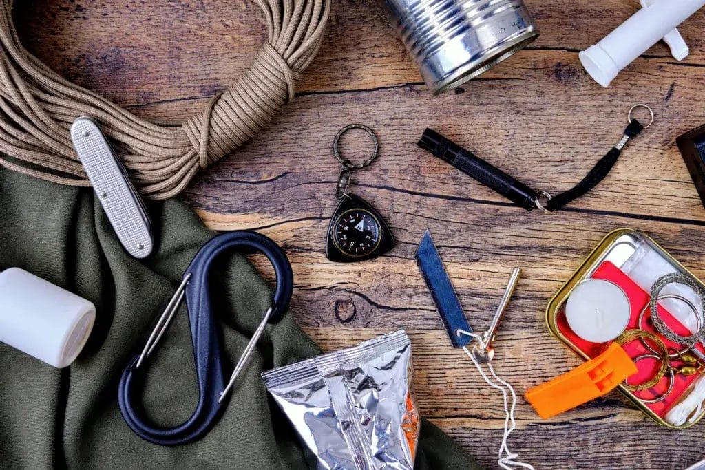 Camping supplies including a carabiner, fire starter kit, compass, twine and whistle.