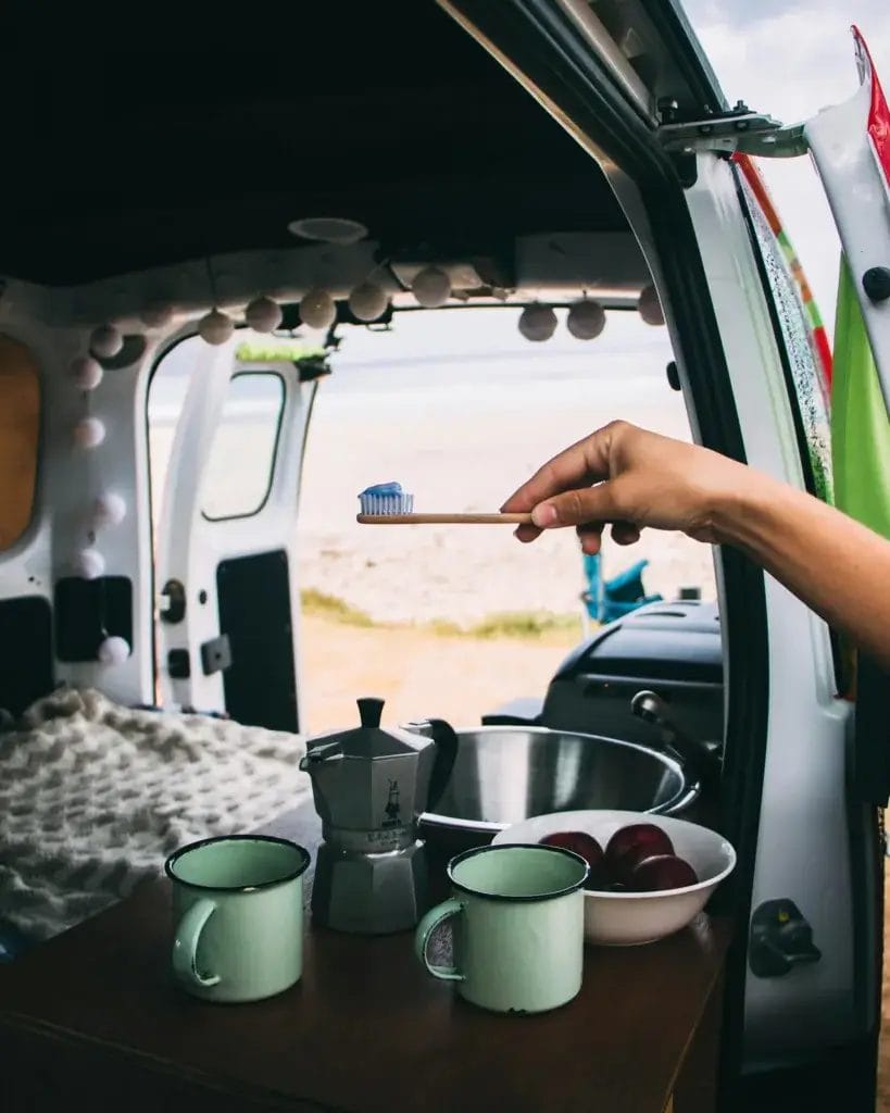 A peaceful morning routine in a campervan by the beach, featuring toothbrush and cups.
