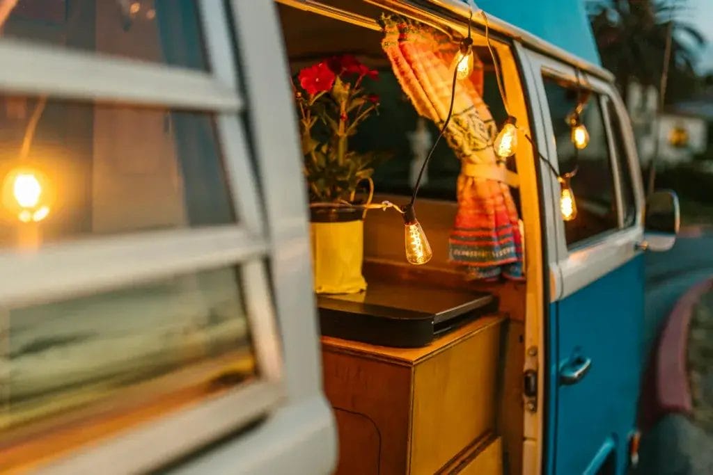 A warm and inviting campervan interior featuring glowing string lights and a potted flower.