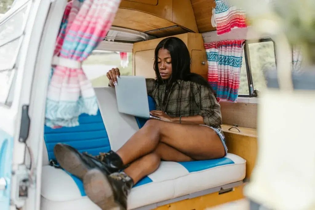 A woman sitting in a camper van using a laptop, enjoying a relaxed mobile workspace.